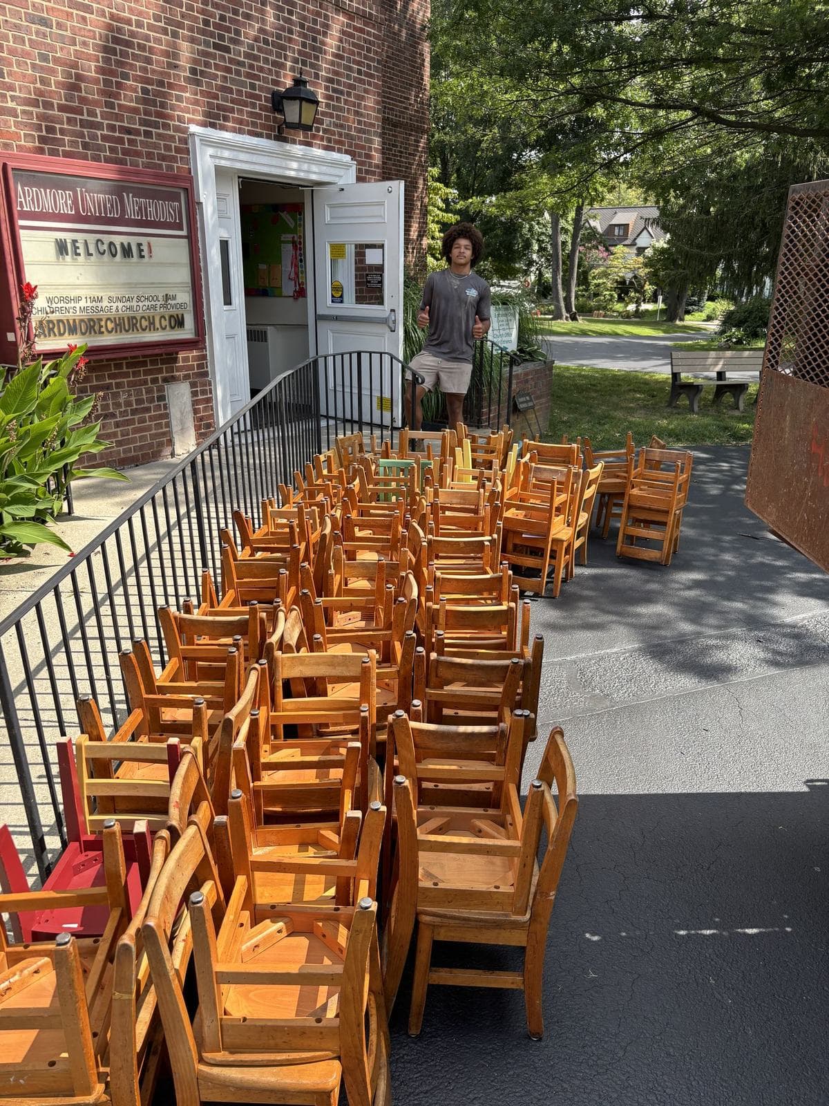 Dozens of wooden chairs stacked outside a building, ready for pickup