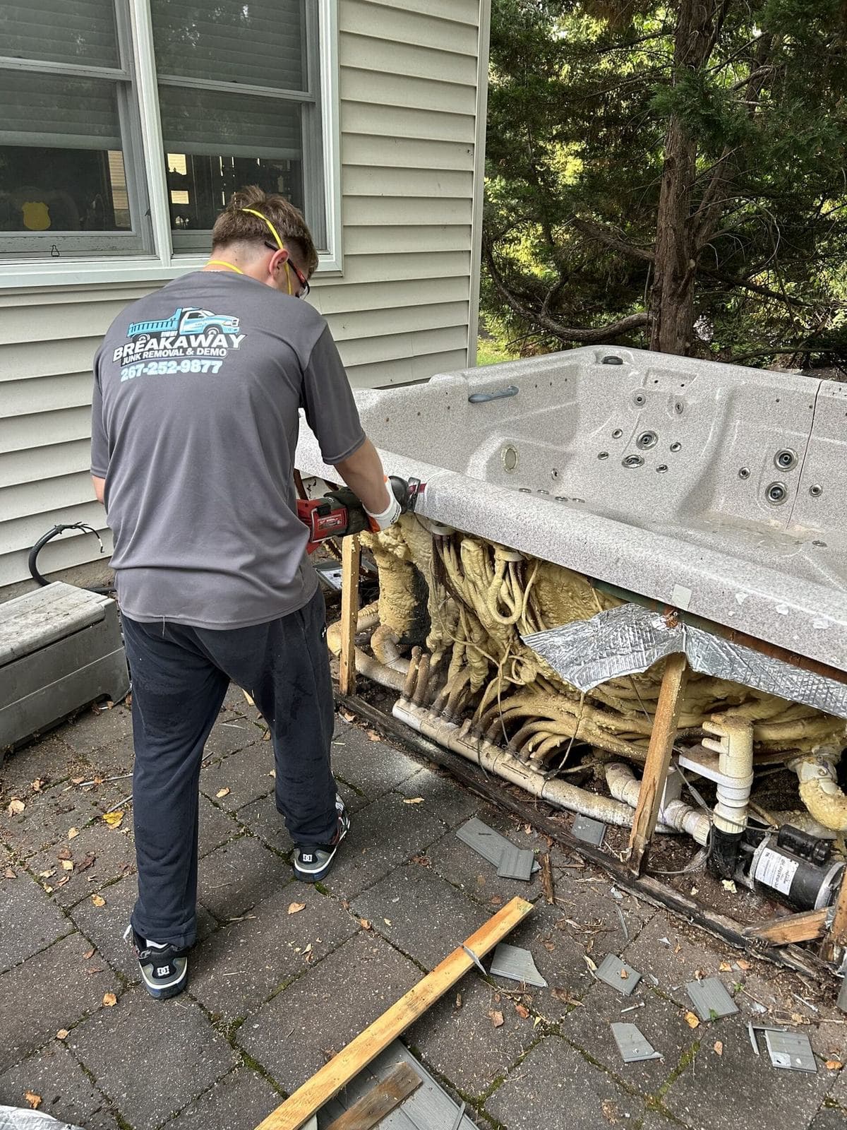 A Breakaway crew member cutting an old hot tub into sections on a patio